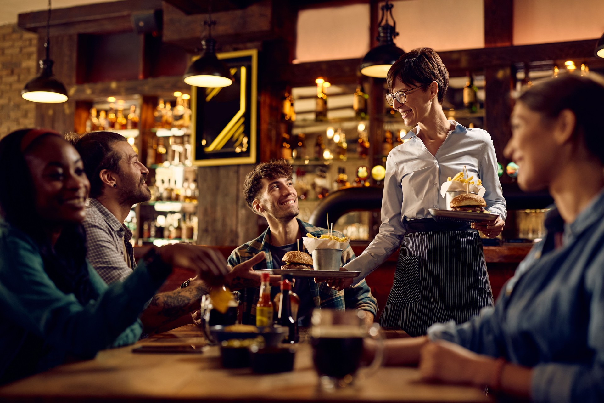 Happy waitress serving food to group of friends in a pub.